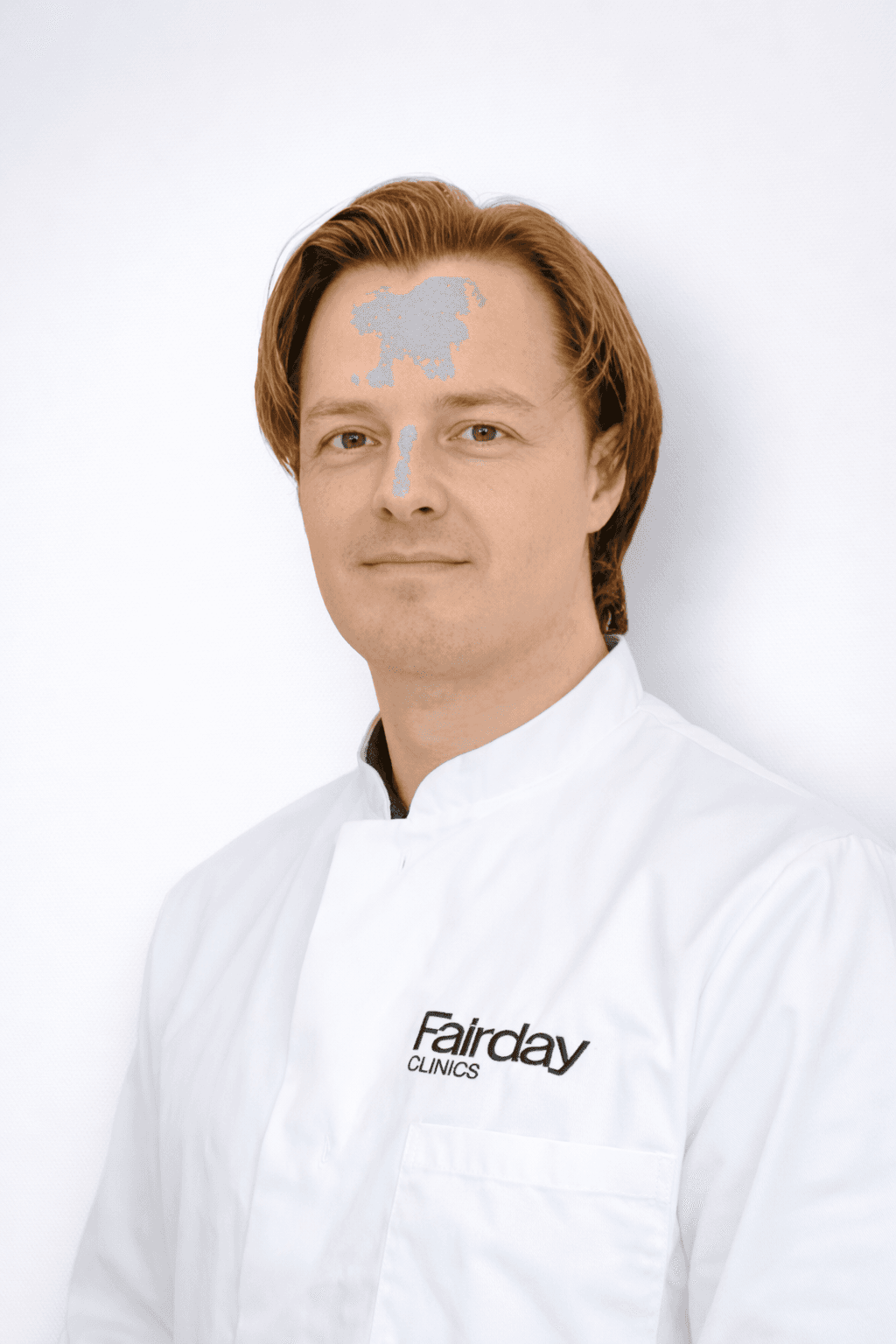 A person in a white coat with "Fairday Clinics" logo stands against a plain background, looking towards the camera.